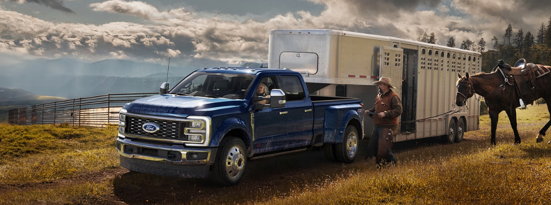 A Ford Super Duty towing a trailer down a rural road next to a horse